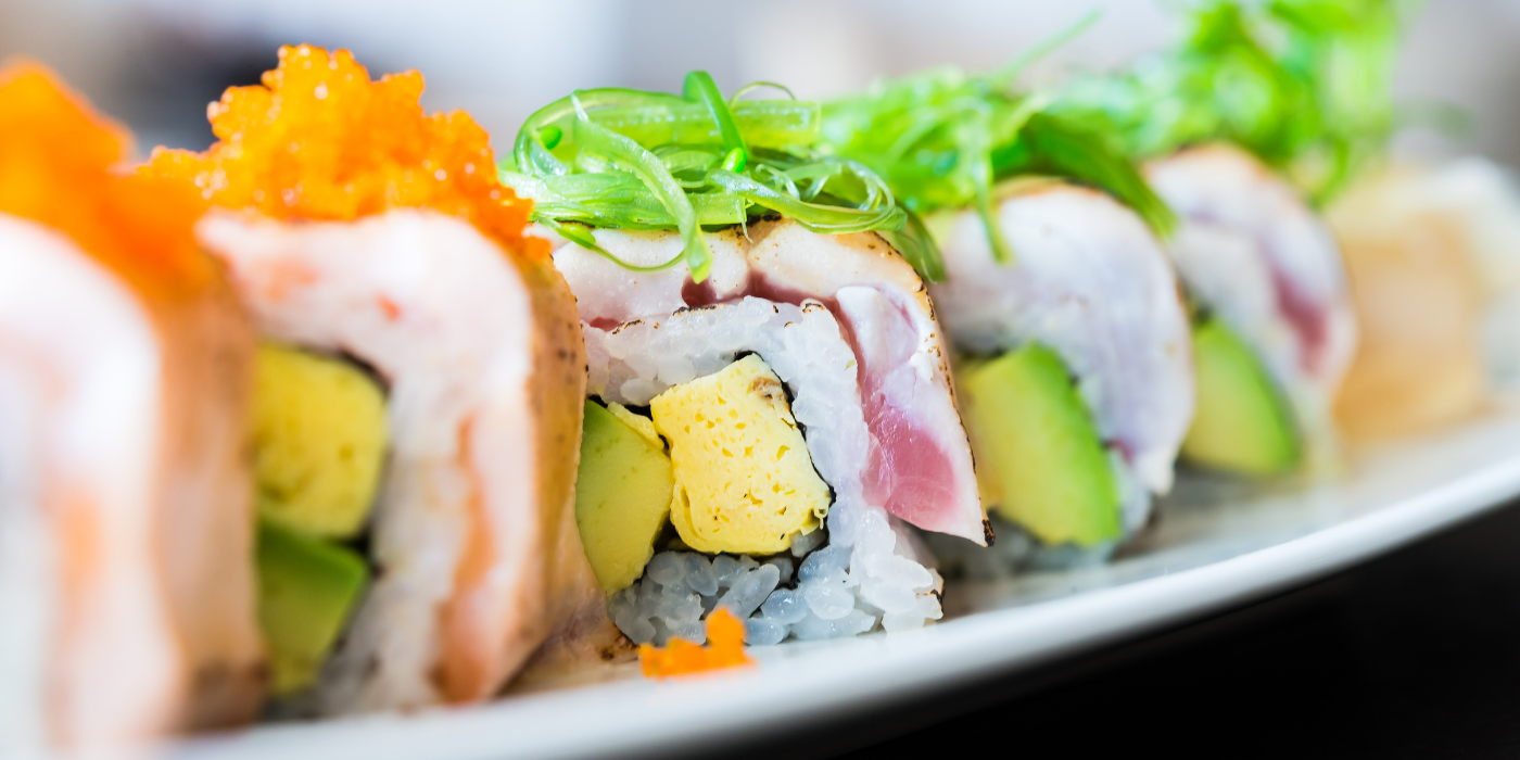 Hero luminoso que introduce la ruta ligera de primavera en el Menú Infinity: makis de salmón en cerámica wabi-sabi, palillos en acción y fondo cálido. Encaja con los bloques de orden de servicio (fríos primero) y con la temática de Sushisom España.