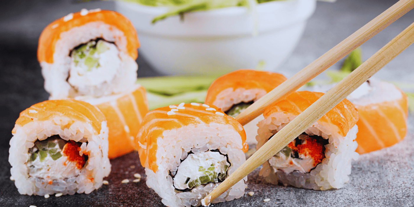 Imagen principal del blog con varios rolls de sushi cubiertos de salmón, acompañados de palillos y presentados en primer plano. Transmite frescura, ligereza y atractivo visual, alineándose con el enfoque del artículo sobre qué pedir en verano dentro del M