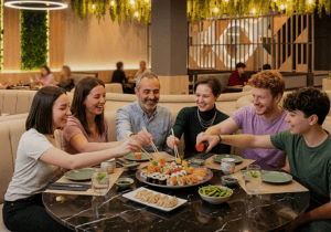 Mesa familiar compartiendo sushi, platos calientes y opciones japonesas al centro. Refuerza la idea de disfrutar sushi en familia dentro del Menú Infinity de Sushisom, con una experiencia cómoda, variada y pensada para compartir.