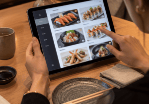 Imagen interna del blog con una persona utilizando una tablet para elegir sushi y otros platos japoneses desde la mesa. Refuerza la experiencia de una primera visita a Sushisom, donde el pedido se realiza de forma cómoda y visual dentro del Menú Infinity.