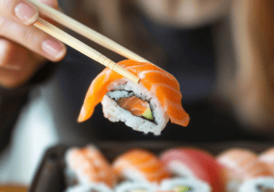 Imagen principal del blog con una persona sujetando una pieza de sushi con palillos antes de probarla. Refuerza la idea de vivir la primera vez en Sushisom sin miedo, empezando con curiosidad y disfrutando el sushi de forma sencilla y natural.